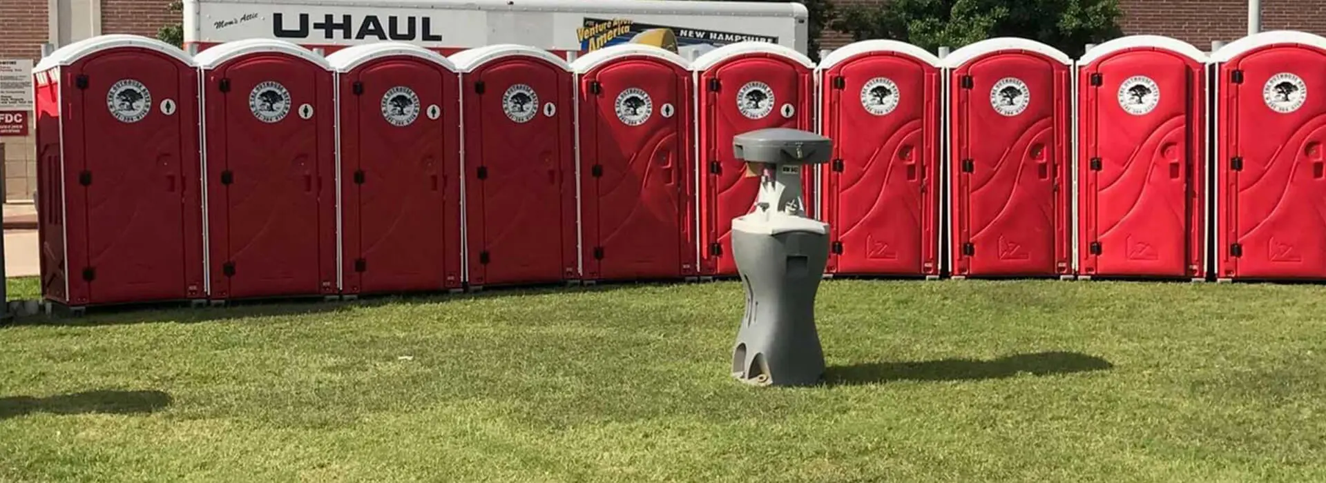 A red and white portable toilet sitting in the grass.