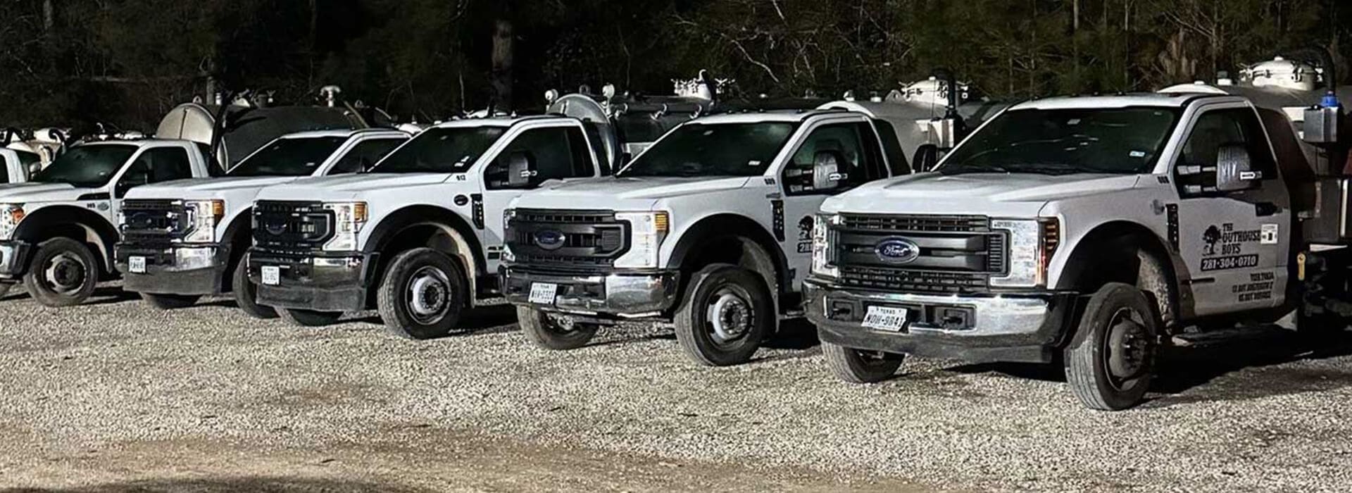 A row of white trucks parked in the dirt.