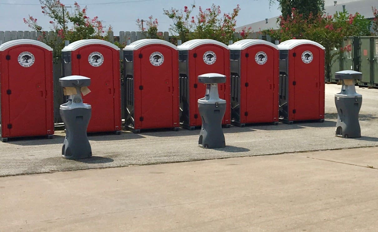 A row of red portable toilets lined up on the side of road.